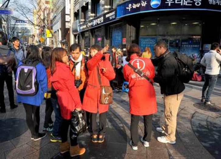 Turistas extranjeros departen en Seúl con guías turísticas locales, vestidas de rojo. (Kim JAE-HWAN/AFP PHOTO)