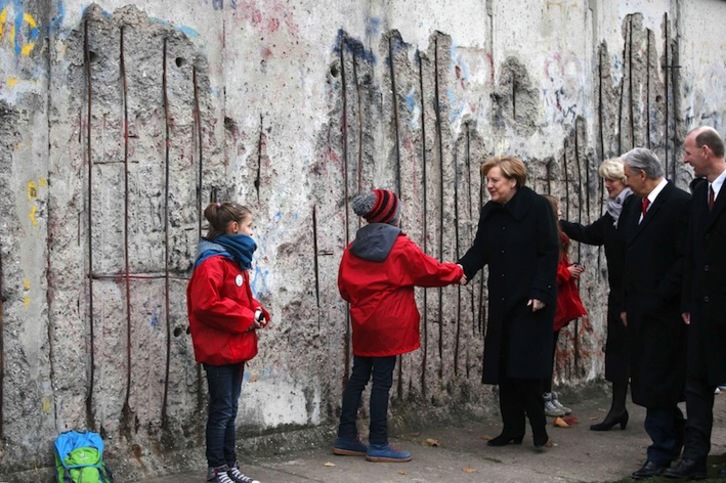 Merkel saluda a dos niñas en su visita a la parte del muro de Berlín que se conserva. (Fabrizio BENSCH/AFP) 