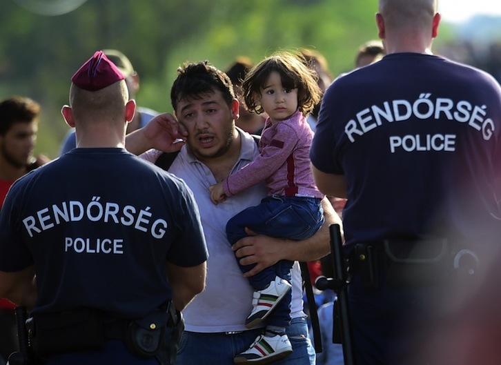 Un refugiado, con una niña en brazos, se topa con la Policía húngara en la frontera. (Attila KISBENEDEK / AFP) 