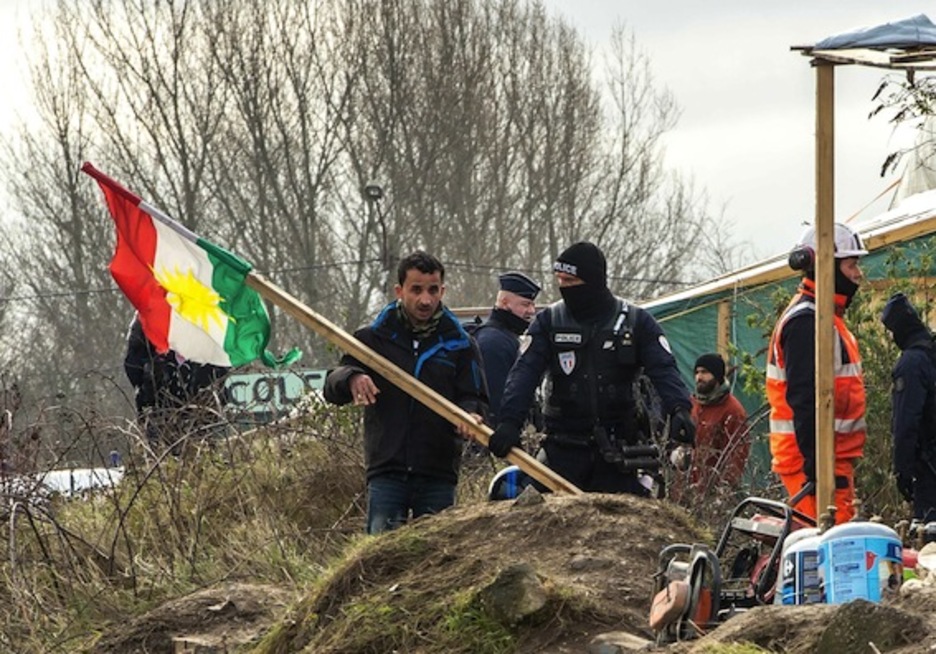 Un refugiado kurdo con una bandera kurda, junto a un agente. (Philippe HUGUEN/AFP) 