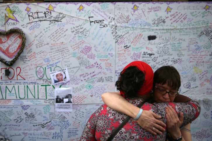 Dos mujeres se abrazan junto a un muro con fotos y mensajes de condolencia. (DANIEL LEAL-OLIVAS / AFP)