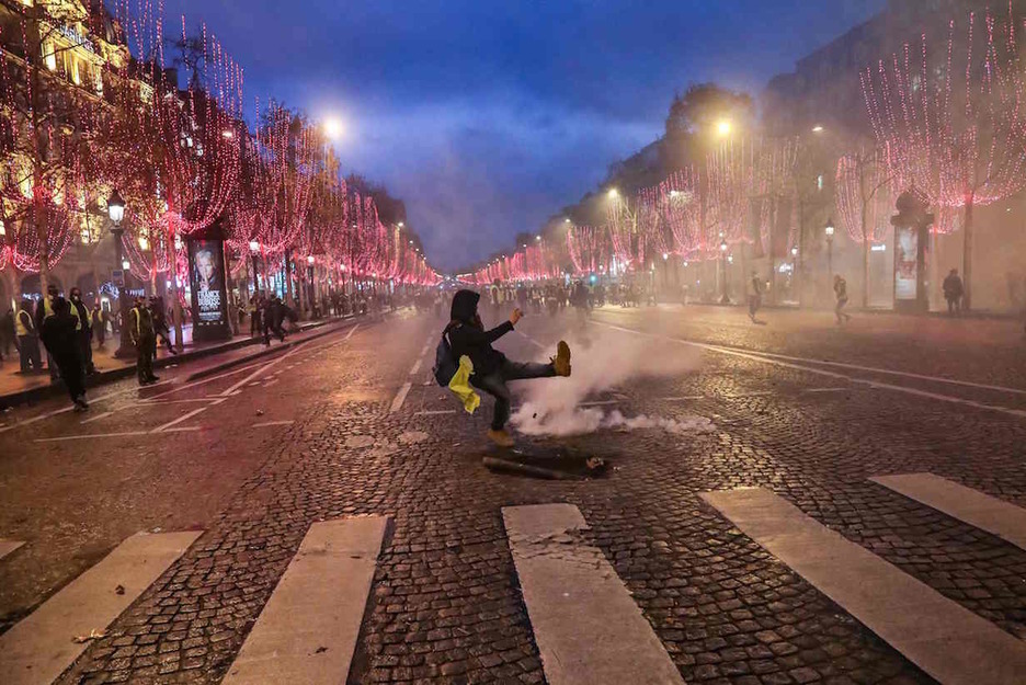 Un manifestante patea un bote de humo entre luces navideñas en París. (ZAKARIA ABDELKAFI / AFP)