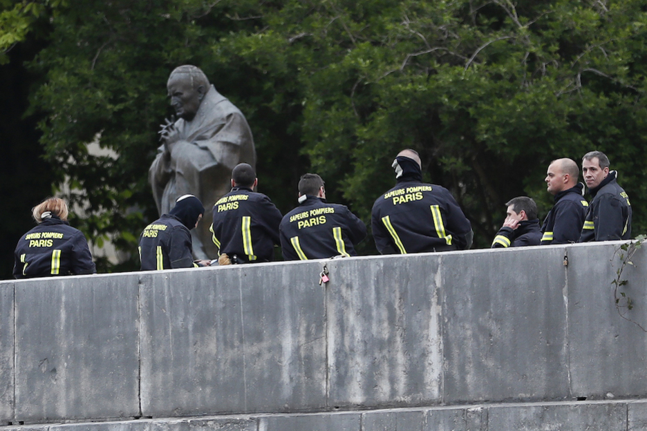 Bomberos se toman un respiro junto a la estatua de Juan Pablo II. (Zakaria ABDELKAFI / AFP)