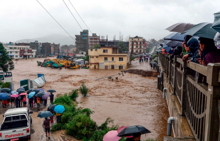 Un montón de curiosos observan la calle asolada por el agua. (Prakash MATHEMA / AFP)
