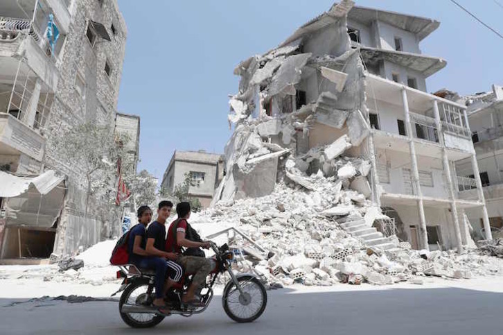 Tres jóvenes pasan junto a un edificio destruido en un bombardeo en Ariha, en Idleb. (Omar HAJ KADOUR/AFP)