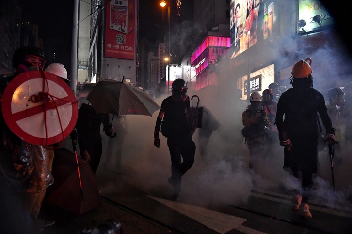 Manifestantes caminan a través de una nube de gases lacrimógenos mientras ocupan Hennessy Road. (Lillian SUWANRUMPHA | AFP)