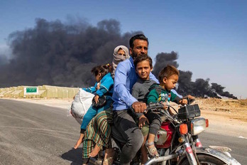 Una familia kurda huye en moto de los combates en Serekaniye, donde los kurdos provocan humaredas para obstaculizar los bombardeos turcos. (Delil SOULEIMAN/AFP)