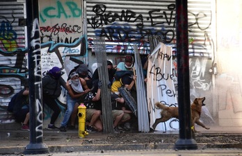 Un grupo de manifestantes se protegen del agua a presión lanzada por los agentes antidisturbios. (Martón BERNETTI/AFP)