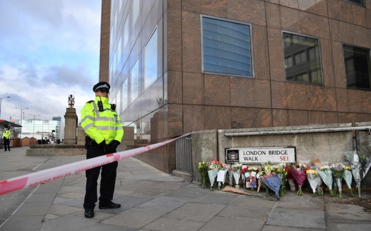 Un policía británico hace guadia junto a la ofrenda floral y el cordón que cierra el paso al Puente de Londres. (Ben STANSALL / AFP)