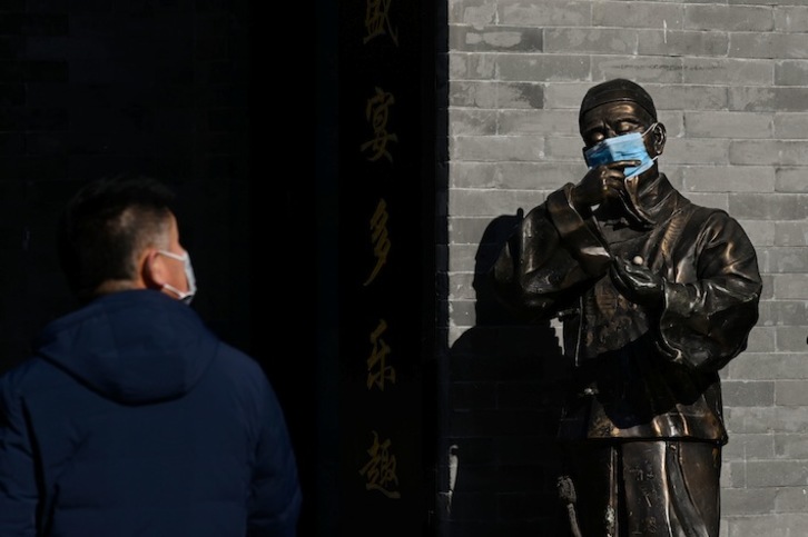 Un hombre observa una estatua de bronce protegida con una mascarilla en Pekín. (WANG Zhao / AFP)