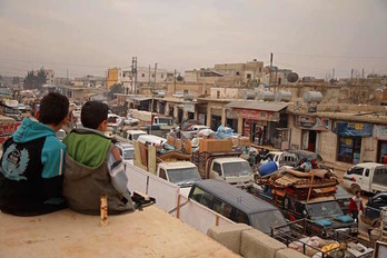 Dos niños obsevan la caravana de vehículos de personas que huyen de los combates en la localidad de Hazano.(Aaref WATAD/AFP)