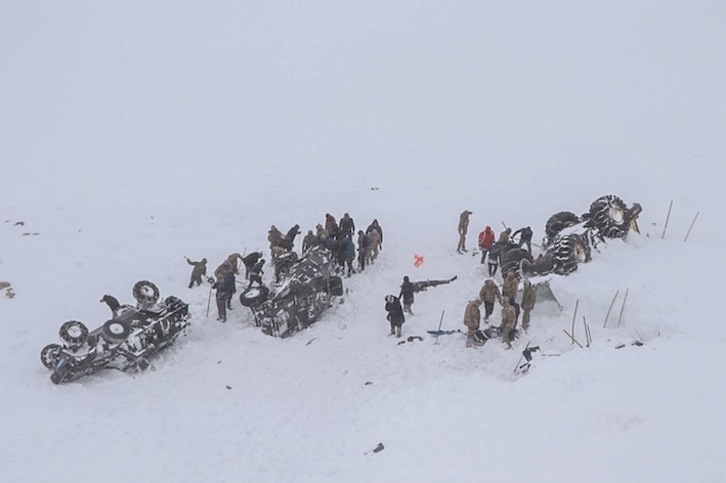 Miembros de los servicios de emergencia trabajan junto a tres de los vehículos sepultados por el alud. (DHA / AFP)