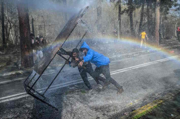 Migrantes se protegen de los cañones de agua de la Policía griega en la zona fronteriza. (Bulent KILIC/AFP)