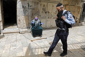 Un policía israelí pasa ante una mujer palestina que reza junto a la Mezquita de Al-Aqsa    (Ahmad GHARABLI I AFP)