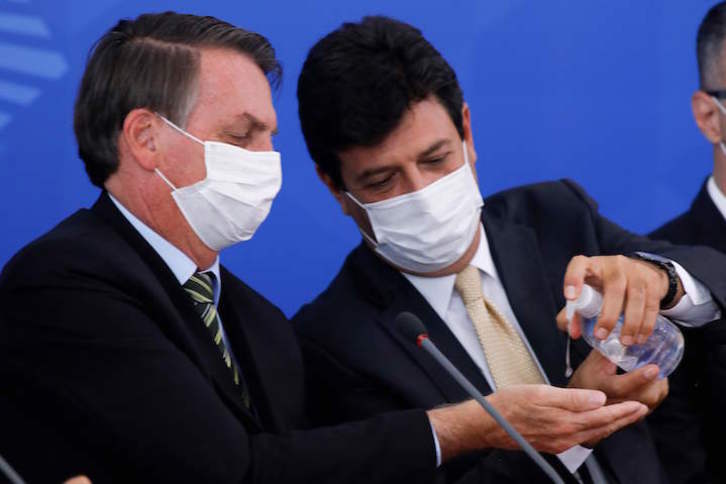 El cesado ministro de Salud, Luiz Henrique Mandetta, aplica gel al presidente brasileño, Jair Bolsonaro, en una rueda de prensa. (Sergio LIMA/AFP)