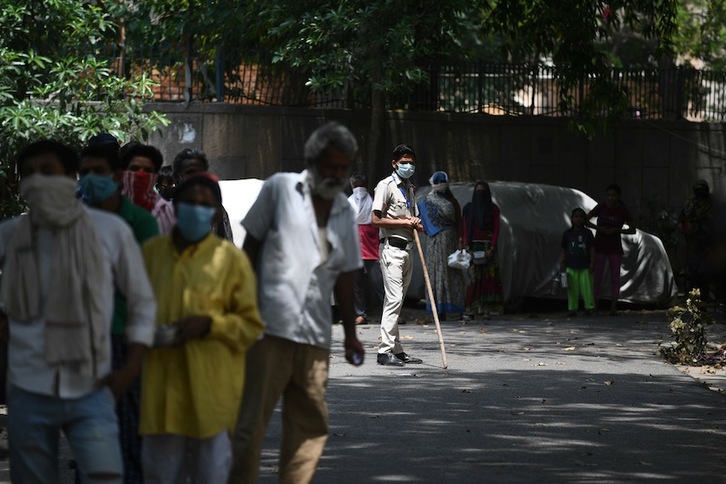 Jendea ahal duen moduan aurpegia estaltzen du makila duen polizia baten ondoan New Delhin. (Autor: Sajjad HUSSAIN/AFP)