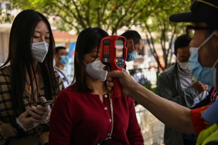 Un trabajador toma la temperatura a dos pasajeras en la estación de Wuhan. (Hector RETAMAL/AFP)
