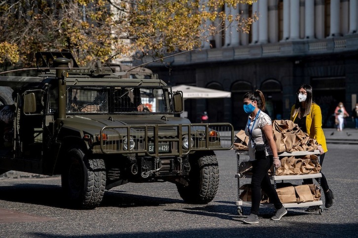 Dos mujeres transportan comida junto a un control militar en Santiago de Chile. (Martin BERNETTI/AFP)