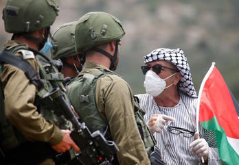 Un palestino ataviado con mascarilla y guantes se enfrenta a soldados israelíes durante una protesta por la Nakba. (Jaafar ASHTIYEH/AFP)