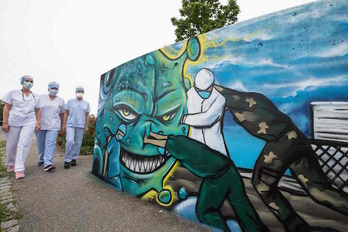 Tres enfermeras pasan junto a un mural que refleja su trabajo contra el coronavirus en el hospital Emilie Muller, en Mulhouse.(Sebastien BOZON/AFP)