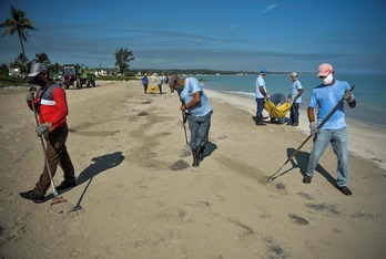 Trabajadores limpian una playa ubicada al este de La Habana. (Yamil LAGE | AFP)