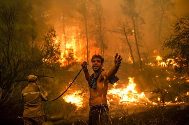 Un residente en la isla griega de Eubea hace un gesto mientras sostiene una manguera durante un intento de extinguir uno de los muchos incendios forestales que están afectando en los últimos días al Mediterráneo oriental. (Angelos TZORTZINIS | AFP)