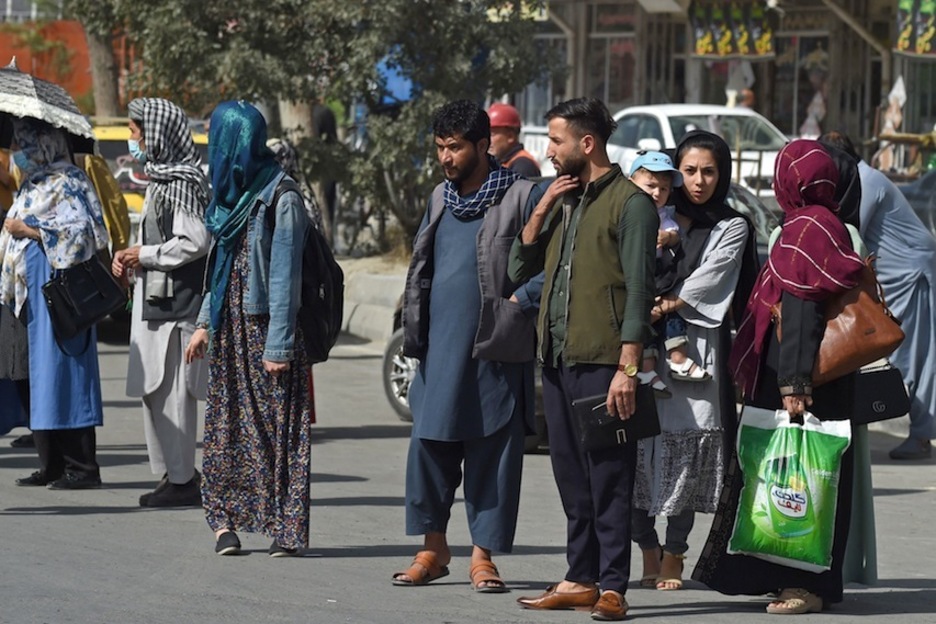 Un grupo de personas esperan un taxi junto a la carretera mientras los talibanes se hacen con el control de la ciudad. (Wakil KOHSAR | AFP)