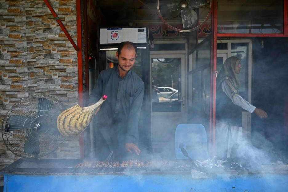 La rutina diaria que no se ha detenido este lunes, 16 de agosto, en Kabul: un vendedor avienta una parrilla mientras prepara unas tradicionales brochetas de carne. (Wakil KOHSAR | AFP)