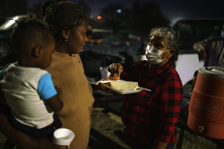 Mexikoko Ciudad Acuñako herritarrek janaria, ura, arropa eta behar dena ematen diete Haititik AEBetara bidean doazen migratzaileei. Irudian, Mari Jaona ageri da Naomi eta David 3 urteko semeari plater bat ematen. (Paul RATJE / AFP)