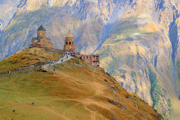 Fotogénica ermita de la Santa Trinidad. Capilla y campanario se alzan desde el siglo XIV sobre una colina a más de 2.200 metros. A sus espaldas el monte Kazbek yergue su inmensa mole.