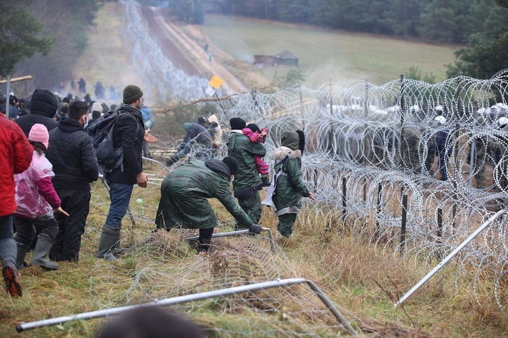 Familias de inmigrantes derriban parte de la alambrada que delimita la frontera de Bielorrusia y Polonia, ante la presencia de los antidisturbios polacos. (Leonid SCHEGLOV/AFP)