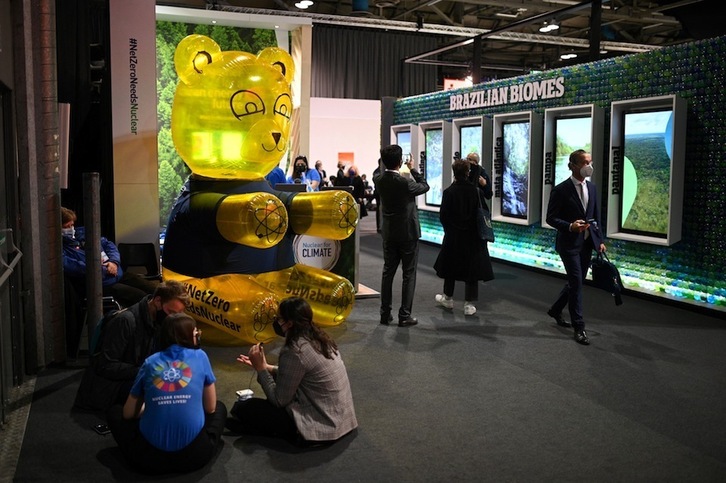 Delegados en la COP26 pasan junto a un stand de la campaña ‘Net Zero Needs Nuclear’, que sostiene que la nuclear es una energía «limpia». (Oli SCARFF/AFP)