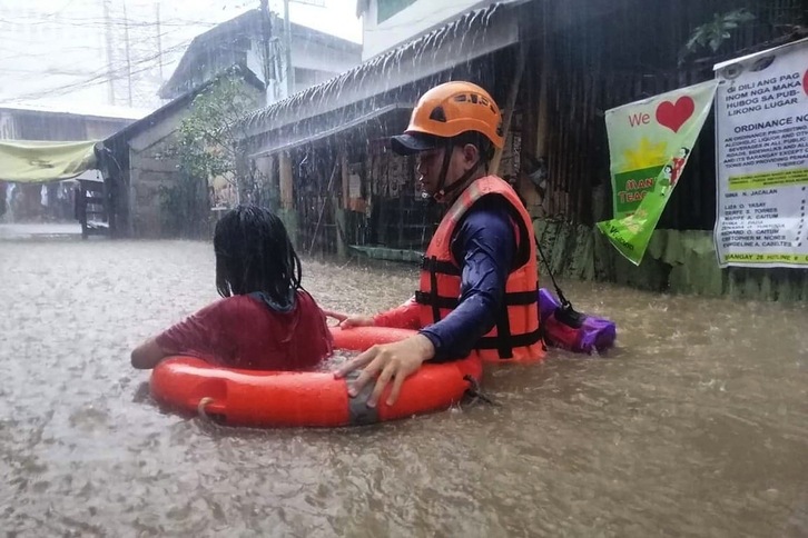 Un miembro de los servicios de emergencia ayuda a una niña a salir de una zona inundada por el tifón Rai en Cagayán de Oro. (HANDOUT/AFP) 