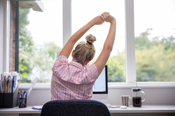 Una mujer realiza ejercicios de estiramiento en su puesto de teletrabajo. 