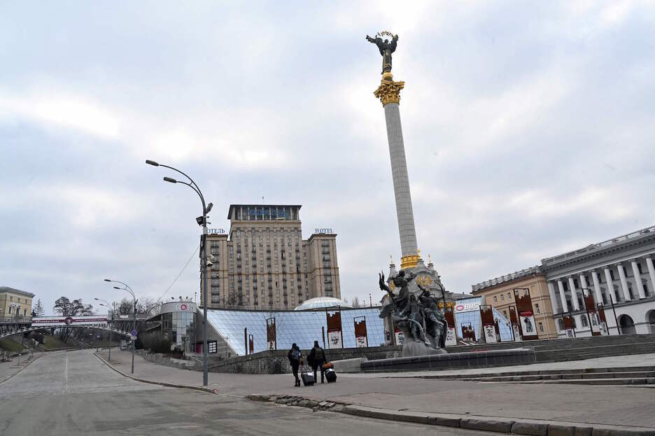 Dos personas, equipaje en mano, caminan por una plaza de la Independencia desierta, en Kiev. 