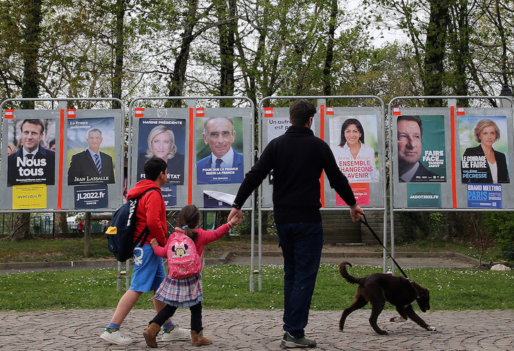 Una familia pasa ante los carteles con los retratos de los candidatos a la elección presidencial, el 1 de abril, en Mugerre.