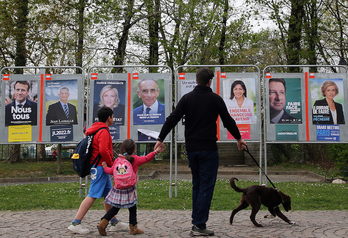 Una familia pasa ante los carteles con los retratos de los candidatos a la elección municipal, el 1 de abril, en Mugerre.