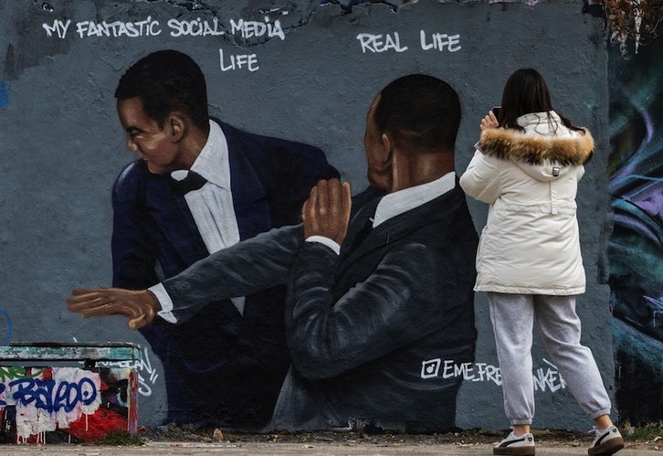 Una mujer fotografía un mural del artista callejero Eme Freethinker, en Berlín, que muestra la imagen más difundida de la última ceremonia de los Oscar.