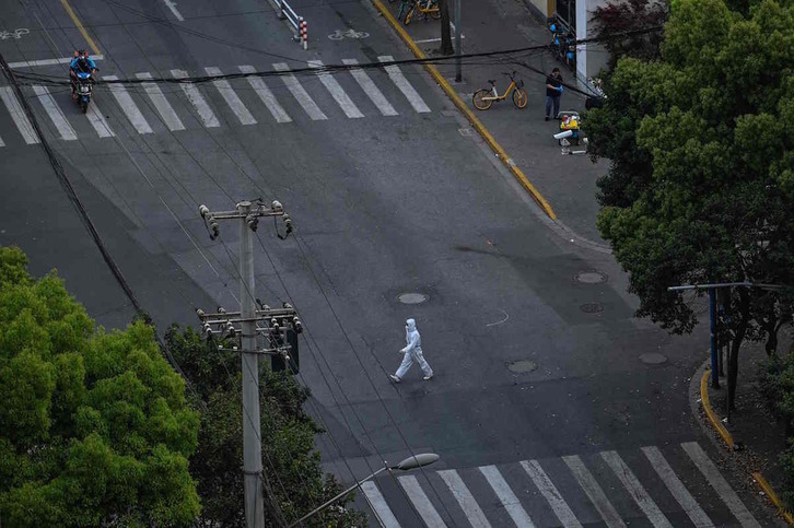 Un sanitario vestido con un EPI pasa por una calle completamente vacía de Shanghai. 