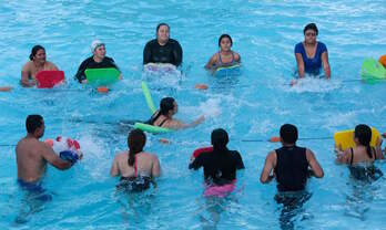 Una mujer nada mientras sus compañeros agitan las aguas de la piscina. 