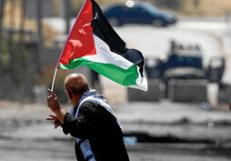 Un palestino ondea una bandera nacional mientras hace el signo de la victoria frente a varios soldados israelíes en la ciudad cisjordana de Beita, al sur de Naplusa, el 3 de junio de 2022.