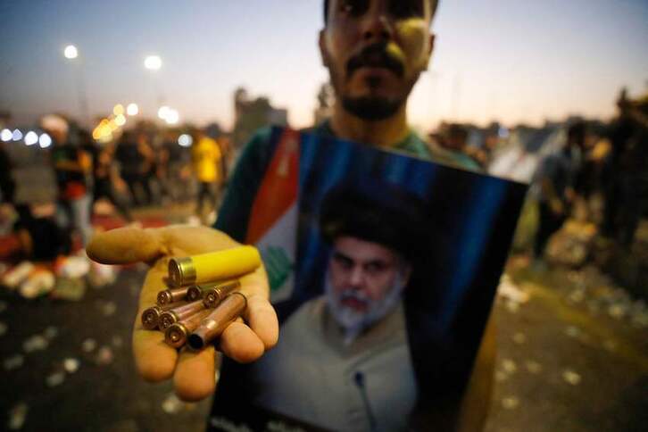 Un seguidor muestra cartuchos recogidos junto al retrato de su líder, Moqtada al-Sadr.