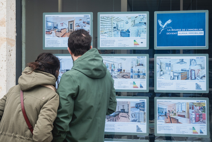 Una pareja joven mira anuncios en una agencia inmobiliaria de Baiona.