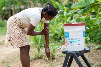 Una joven se lava en Haití con agua de un cubo de ayuda humanitaria. 