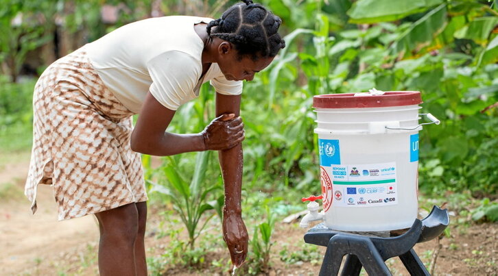 Una joven mujer haitiana se lava con un cubo de agua de ayuda humanitaria.