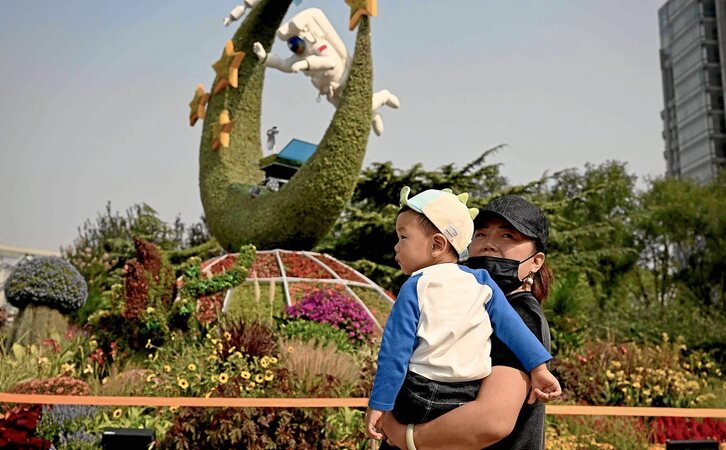 En la imagen de portada de este reportaje, una mujer y su hijo pasan en  Beijing frente a una exposición de flores que representa el programa espacial de China. Fotografía: Noel Celis | AFP 