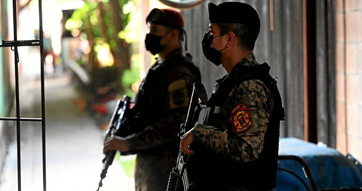 Militares salvadoreños registran una casa en Soyapagngo. Al lado, los activistas salvadoreños Jason García y Azucena Ortíz, de espaldas por razones de seguridad, durante su reciente visita a Madrid.