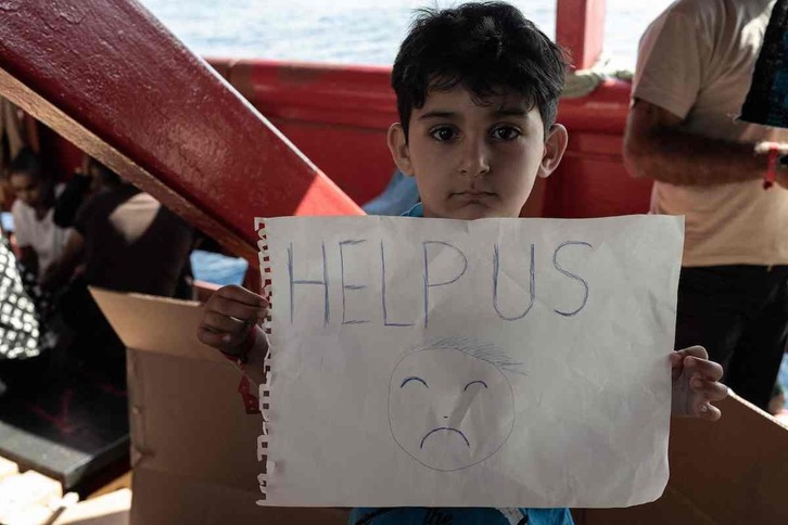 Un niño muestra un cartel pidiendo ayuda tras ser rescatado del mar por SOS Mediterranée.