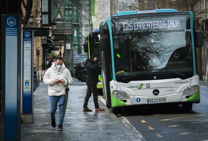 Una persona con mascarilla camina junto a un autobús en Donostia en una imagen de archivo.