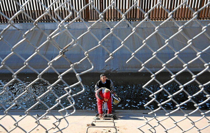 Migrantes pasan un canal tras cruzar por un agujero en la valla fronteriza en El Paso.